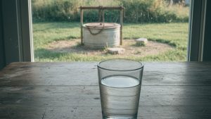 Glass of well water on a kitchen table, private well visible outside