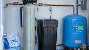 Water softener and brine tank installed beside a well pressure tank in a home utility room